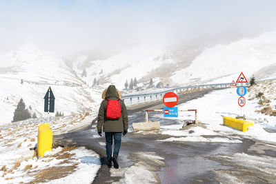 Rear view of person walking on snow covered mountain road against misty sky