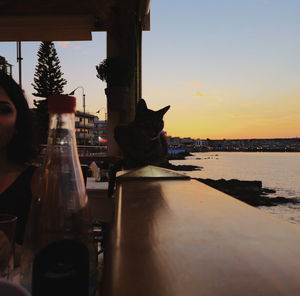 Men sitting at shore against sky during sunset