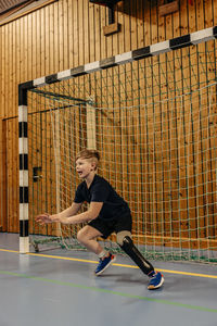 Boy with disability goalkeeping near net while playing football at sports court