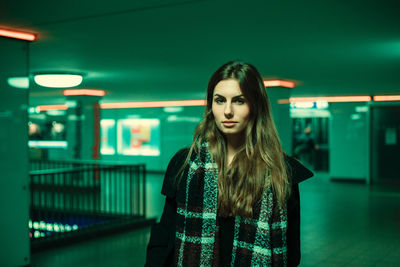 Portrait of young woman standing against illuminated wall