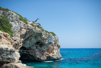 Rock formation in sea against clear blue sky