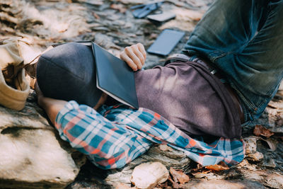 Man with book on face lying on leaves in forest