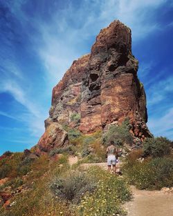 Rear view of shirtless man standing on land against rock formation and sky