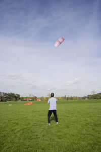 Rear view full length of man flying kite on grassy field against sky