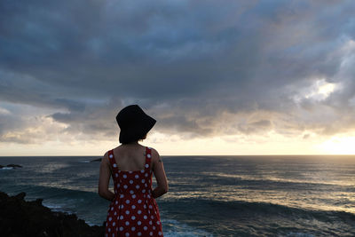 Rear view of woman standing at beach against sky