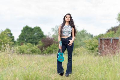 Portrait of young woman holding ukulele while standing on grass