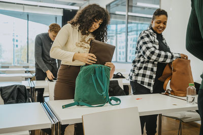 Multiracial students packing backpack in classroom at community college