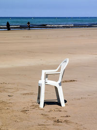 White plastic chair on the beach with few people around