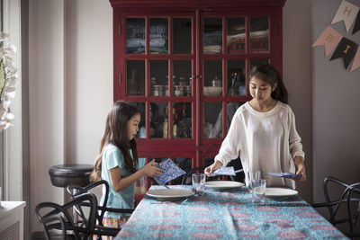 Sisters arranging dining table at home for surprise birthday celebration