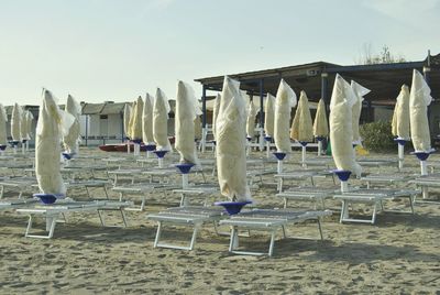 Closed parasols and lounge chairs at beach against clear sky