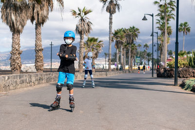 Full length of siblings wearing mask inline skating on road against sky