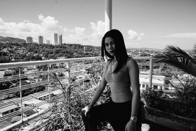 Portrait of beautiful woman standing at balcony against sky