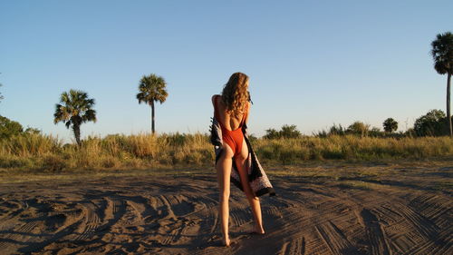 Rear view full length of young woman wearing one piece swimsuit with scarf on sand