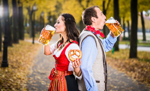 Couple drinking beer while standing at park during autumn
