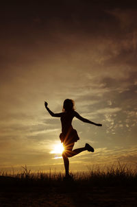 Silhouette woman with arms outstretched on field against sky during sunset