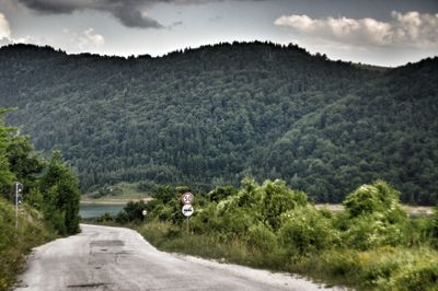 Road amidst trees and mountains against sky