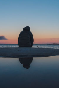 Rear view of person standing at beach against clear sky during sunset