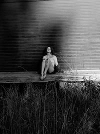 Young woman sitting on wood against brick wall