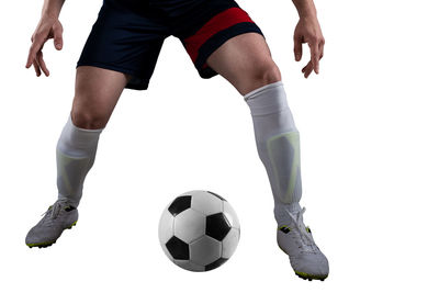 Low section of woman playing soccer ball against white background