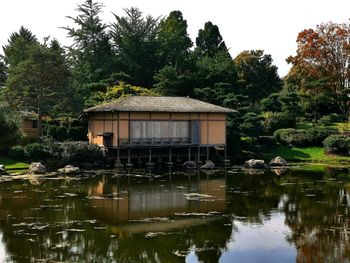 House by lake and trees against sky