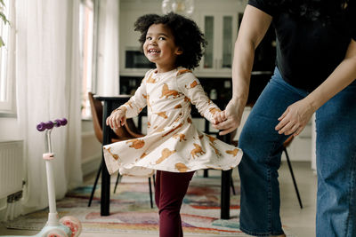 Cheerful daughter dancing with mother in kitchen at home