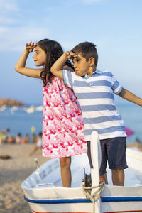 Siblings shielding eyes while standing on boat at beach