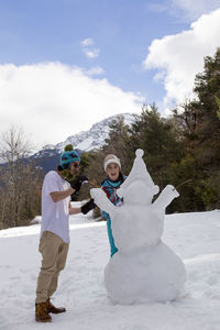 Portrait of siblings making snowman while standing outdoors during winter