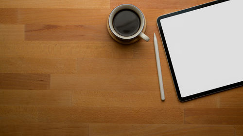 Directly above shot of coffee cup with digital tablet on table