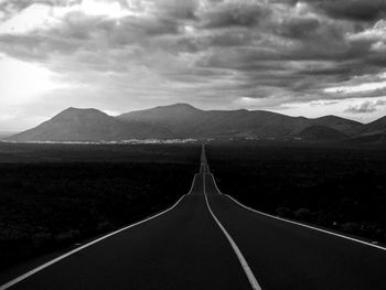 Empty road leading towards mountains against sky