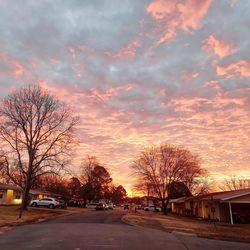 Road by trees against sky during sunset