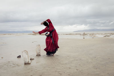 Rear view of woman standing at beach against sky