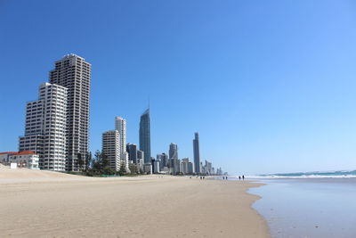 Modern buildings by sea against clear blue sky