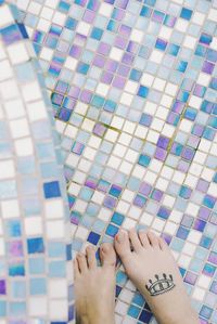 Low section of woman with tattoo on foot standing on tiled floor at poolside