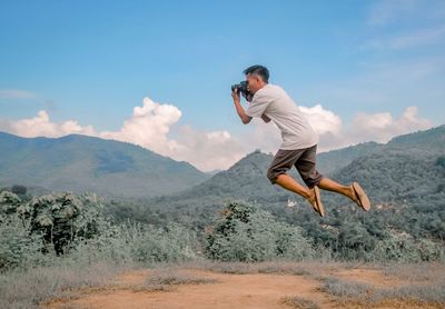 Side view of young man jumping in mountains against sky