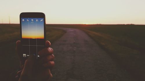 Close-up of hand holding smart phone against sunset