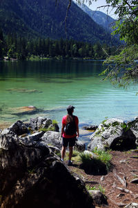 Rear view of man standing on rock by lake