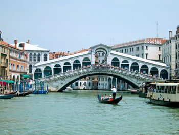 People on arch bridge over canal against clear sky