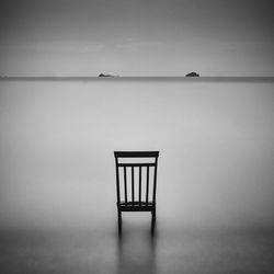 Empty chair at calm sea against the sky
