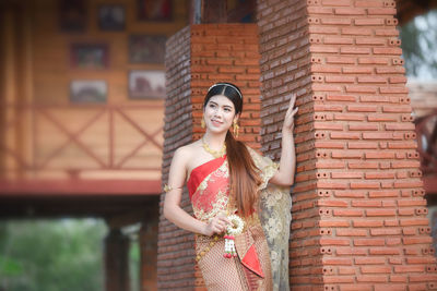 Smiling young woman wearing traditional clothing and jewelry while standing by wall