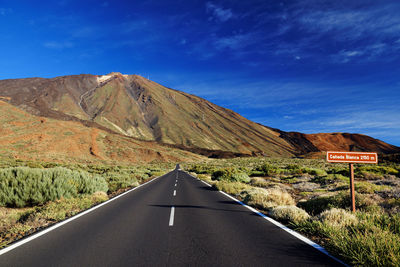 Empty road along rocky landscape against blue sky