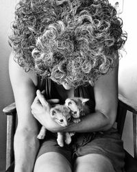 Woman holding cats while sitting on chair against wall