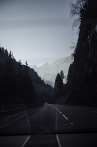 Road by trees against sky seen through car windshield