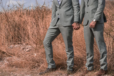 Low section of gay couple wearing suit standing on field