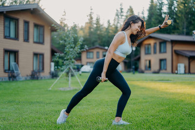 Side view of smiling woman lifting dumbbells on grassy land