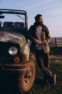 Full length of young man standing by car on field