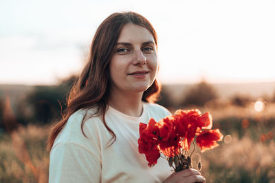 Portrait of woman holding red flowering plant against sky