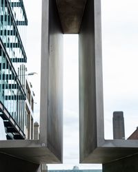 Low angle view of bridge by buildings against sky