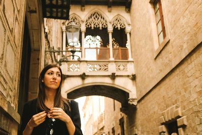 Young woman looking away while standing against building