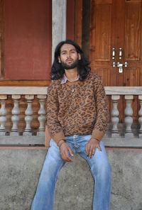 A sexy handsome young man with long hair style looking at camera while sitting in old temple