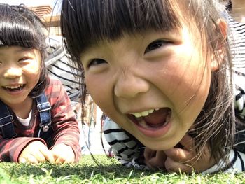 Close-up of playful girl shouting while lying with sister on grassy field